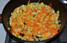 Убрав огонь до среднего, засыпаем в сковороду шинкованный крупным кубиком лук, морковь,  пассеруем  6-7 минут. 